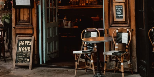 Außenbereich eines Gastronomiebetriebs mit Tischen, Stühlen und einer Tafel mit Happy Hour