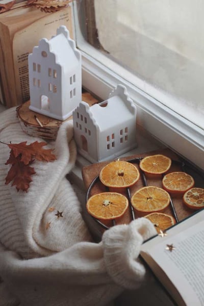 Fensterbank im Winter mit Pullover, Orangenscheiben, Büchern und Holzdekoration