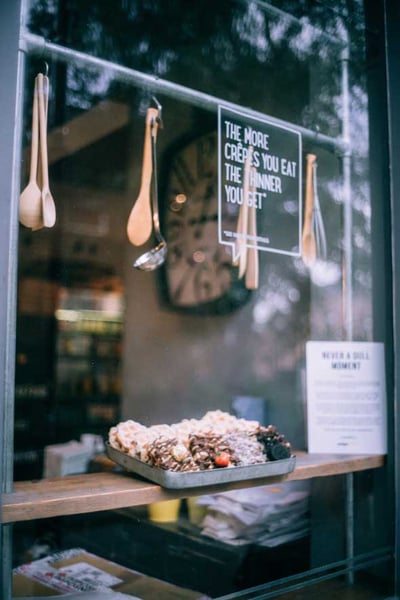 Kekse und anderes Gebäck liegen in einem Blech auf einem Holzbalken im Schaufenster in einem Crepes-Laden