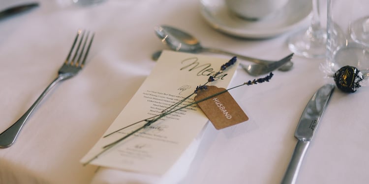 Eine Menükarte für den Ehemann liegt zwischen Messer und Gabel auf dem weißen Hochzeitstisch