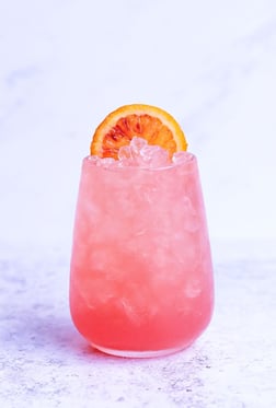Trendgetränk in pinker Farbe mit Eiswürfeln und einer Orangenscheibe