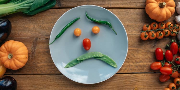Teller mit Gemüse, welches ein Gesicht bildet auf einem Holztisch