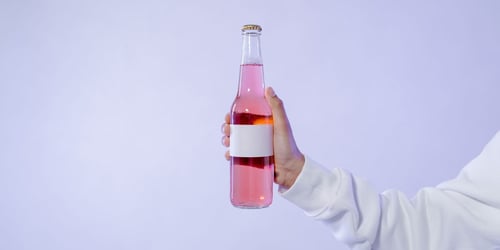 Eine Hand hält rosa Flüssigkeit in einer Glasflasche, ein fertiger Cocktails für die Gastronomie