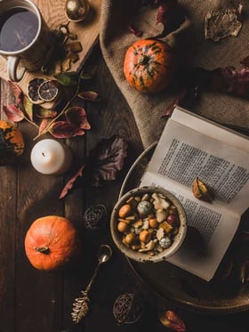 Herbstatmosphäre mit einem offenen Buch, einem Kürbis und Snacks