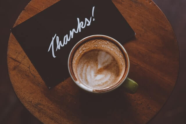 Eine Karte mit "Thanks" und eine Tasse Kaffee auf einem kleinen Bistro-Tisch