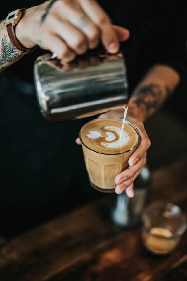 Kellner schenkt einen MIlchkaffee in ein Glas