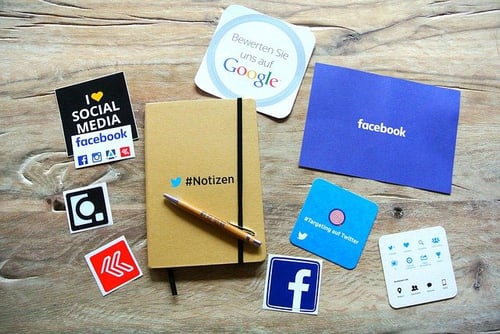 Ausgedruckte Social Media App Logos auf einem Holztisch mit Notizbuch